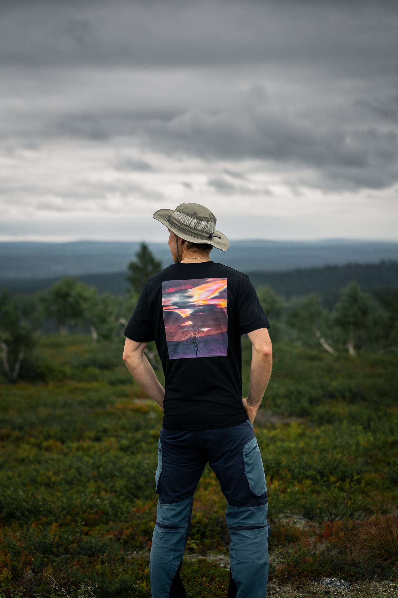 Back view of the eco-friendly Novapuro x Jetro Luhtaa black t-shirt showcasing a colorful midnight sun landscape graphic on organic cotton.