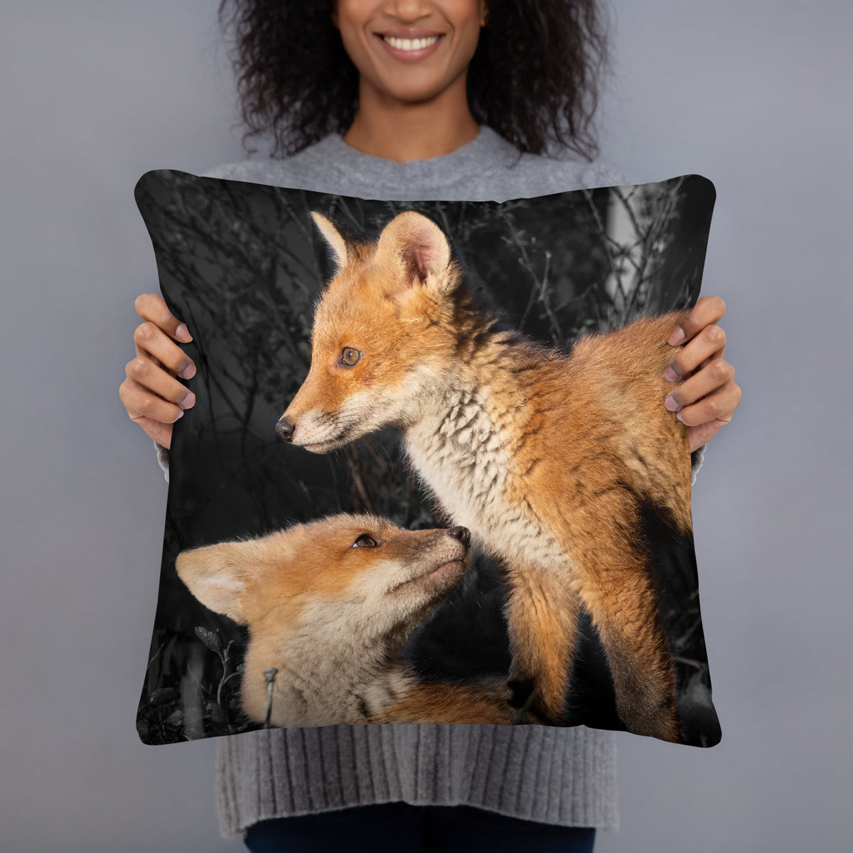 Novapuro x Auli Leivonen dark decorative throw pillow featuring two playful Nordic fox kits, resting on a dark sofa with a green cozy blanket.