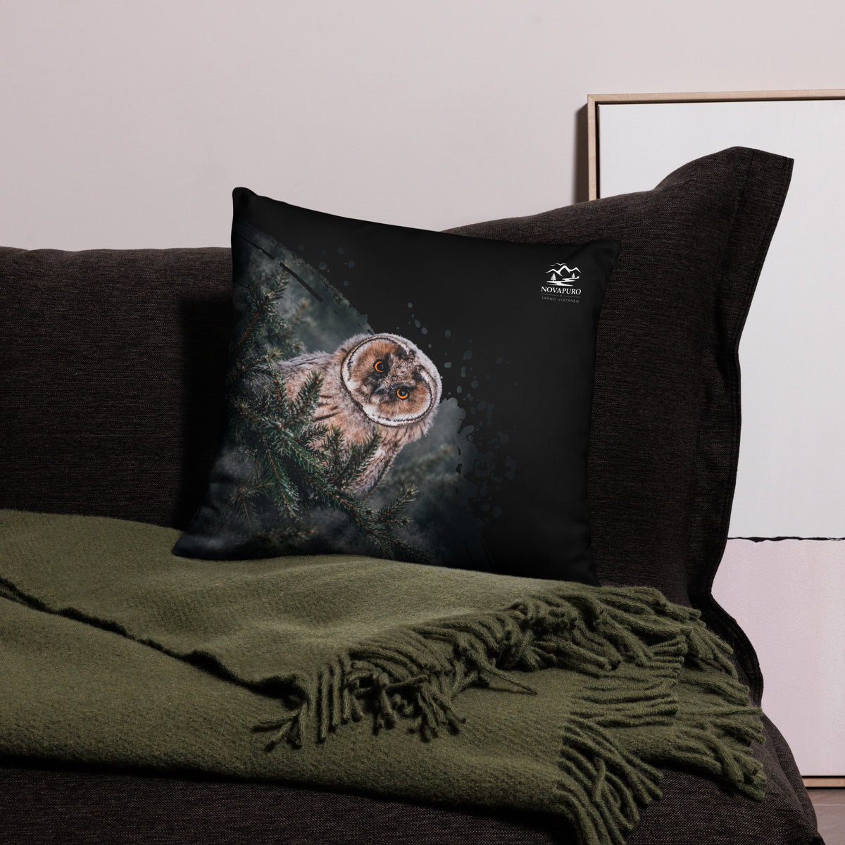 A black accent throw pillow featuring a Nordic long-eared owl chick print by Jarno Virtanen, resting on a bed.