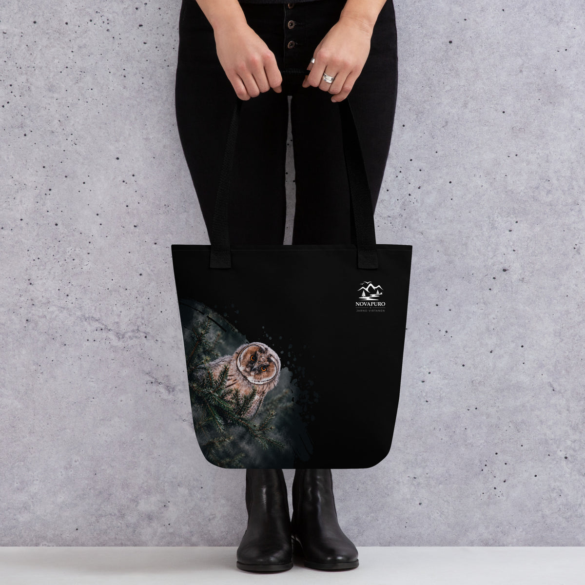 A person carrying the black Novapuro x Jarno Virtanen tote bag featuring a Nordic long-eared owl chick print on the lower side.