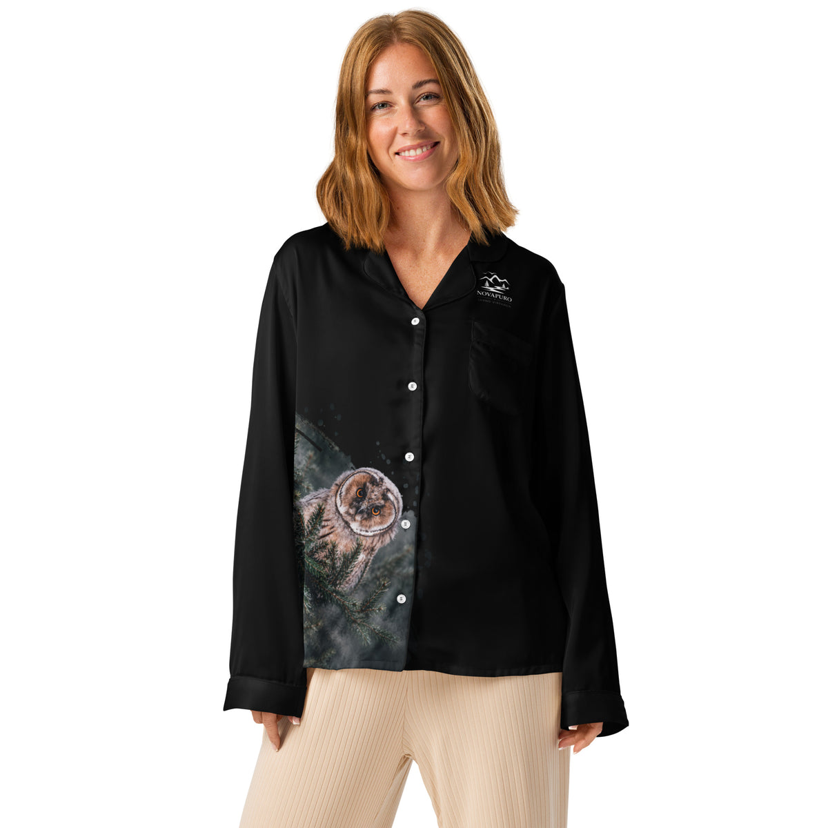 A woman wearing the black Novapuro x Jarno Virtanen long sleeve pajama top featuring a Nordic long-eared owl chick print on the lower side, standing in a cozy room.