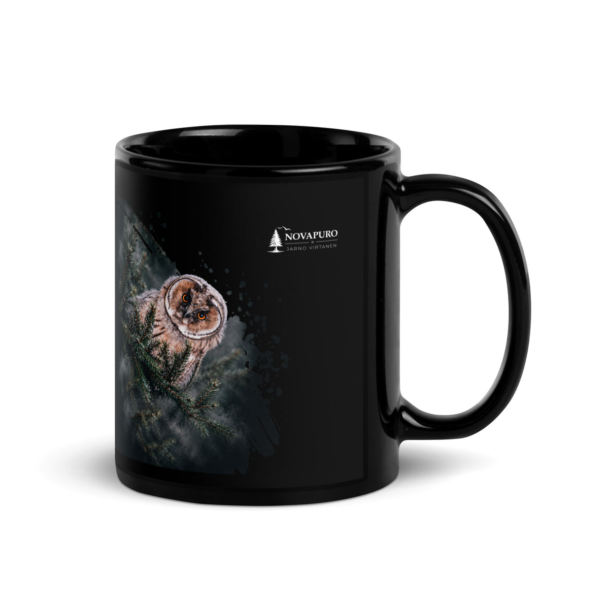 A black glossy ceramic mug featuring a Nordic long-eared owl chick print by Jarno Virtanen, sitting on a desk next to a notebook.