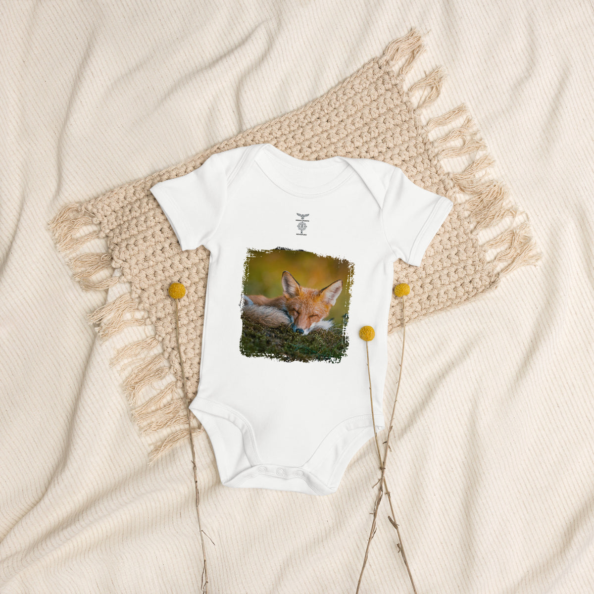 A baby bodysuit featuring an original photograph of a resting red fox in the morning sun by Mikko Monto, displayed in a natural setting