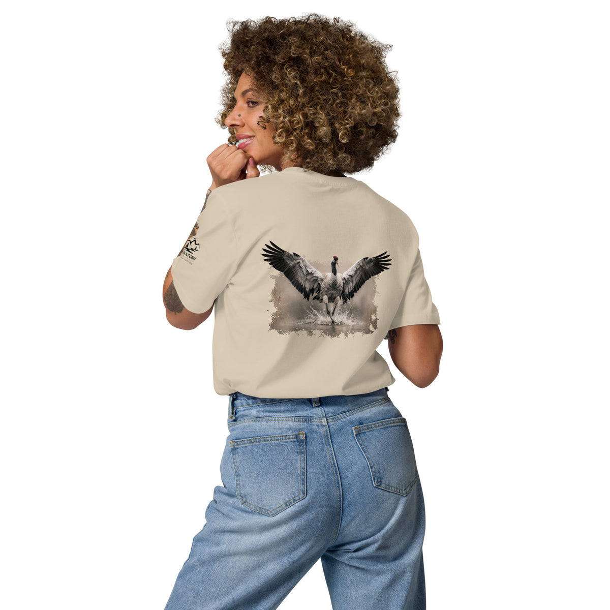 Woman wearing a sustainable organic cotton t-shirt in beige, featuring a minimalist Nordic wildlife graphic of a dancing crane by Jarno Virtanen. Perfect for nature lovers.