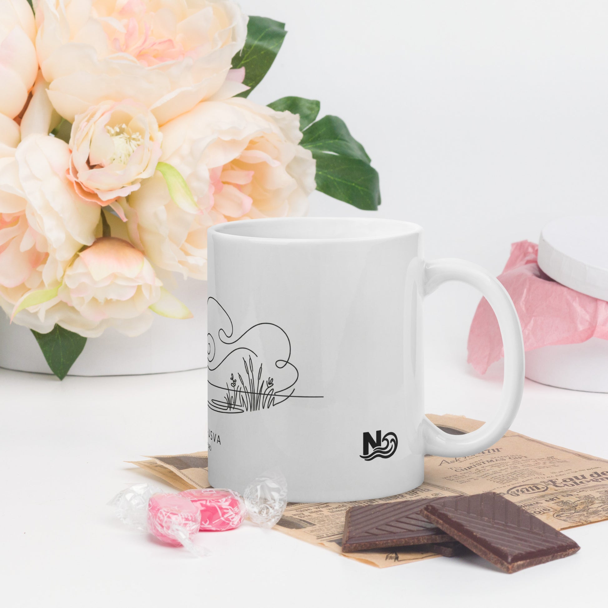 A white glossy coffee mug featuring a minimalist continuous black line illustration of morning mist over a Nordic lake, with the Finnish text "AAMU-USVA" below it.