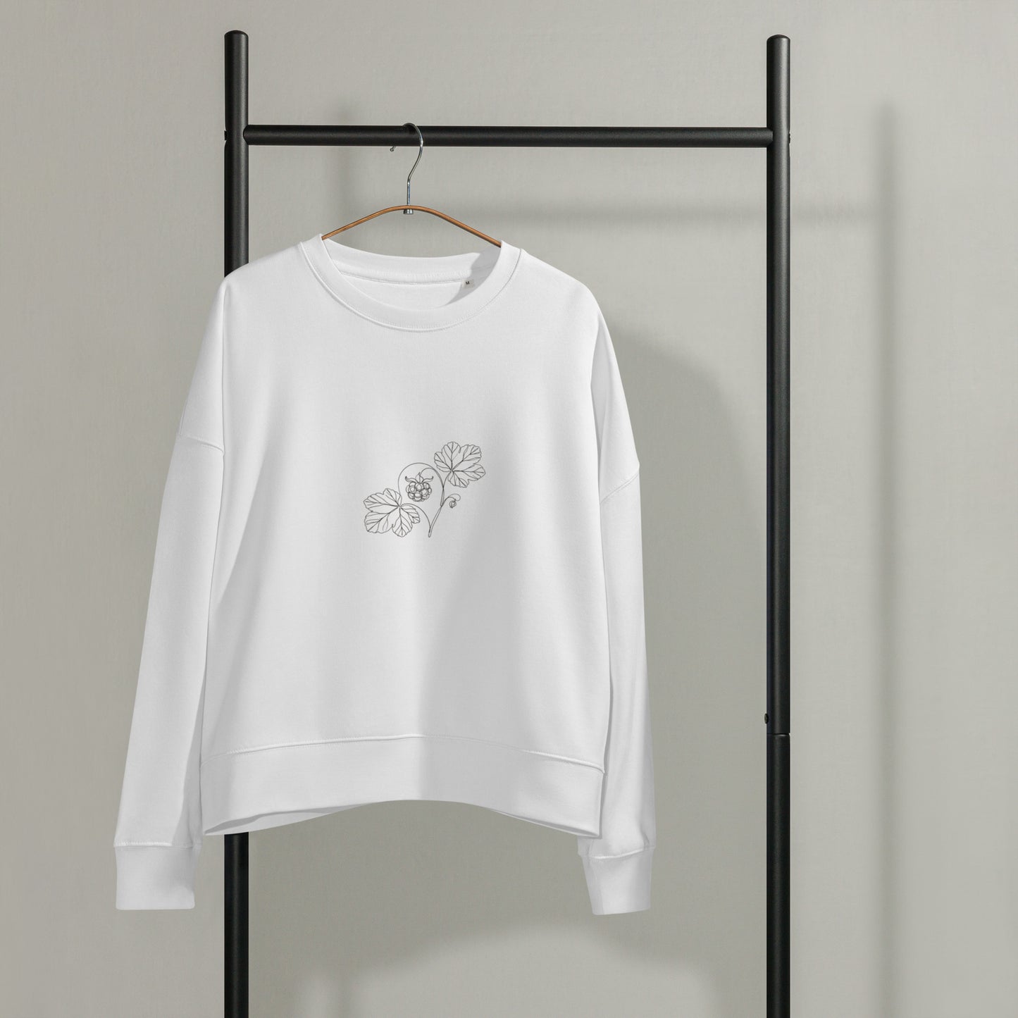 White Novapuro women's organic cotton crewneck sweatshirt hanging on a black garment rack, featuring a minimalist botanical cloudberry line art illustration on the left chest