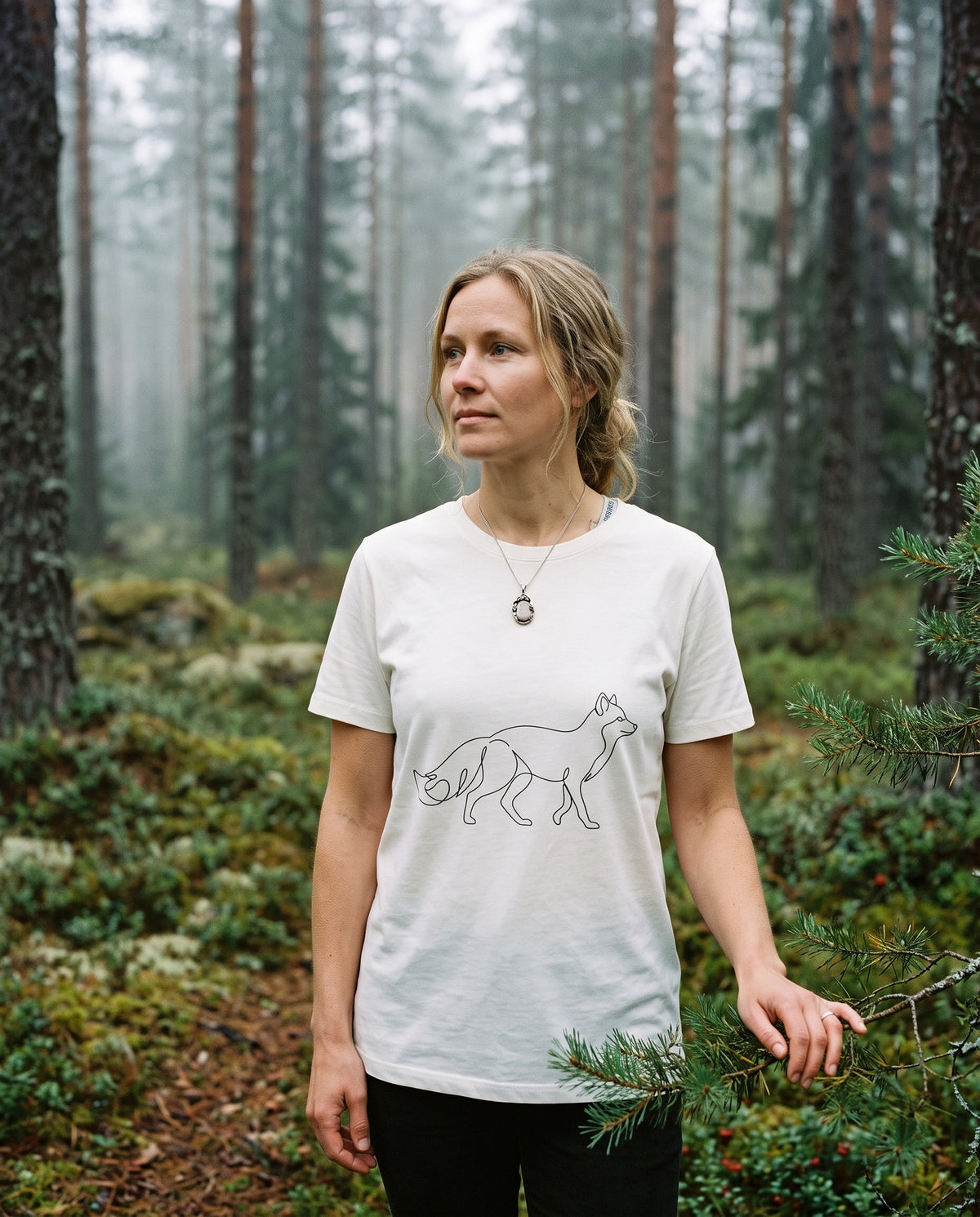 A woman enjoying the Nordic nature wearing Novapuro's off-white women's organic cotton Arctic Fox t-shirt. This ecological and sustainably made tee with a minimalist arctic fox print offers breathable comfort for both outdoor adventures and casual everyday wear.